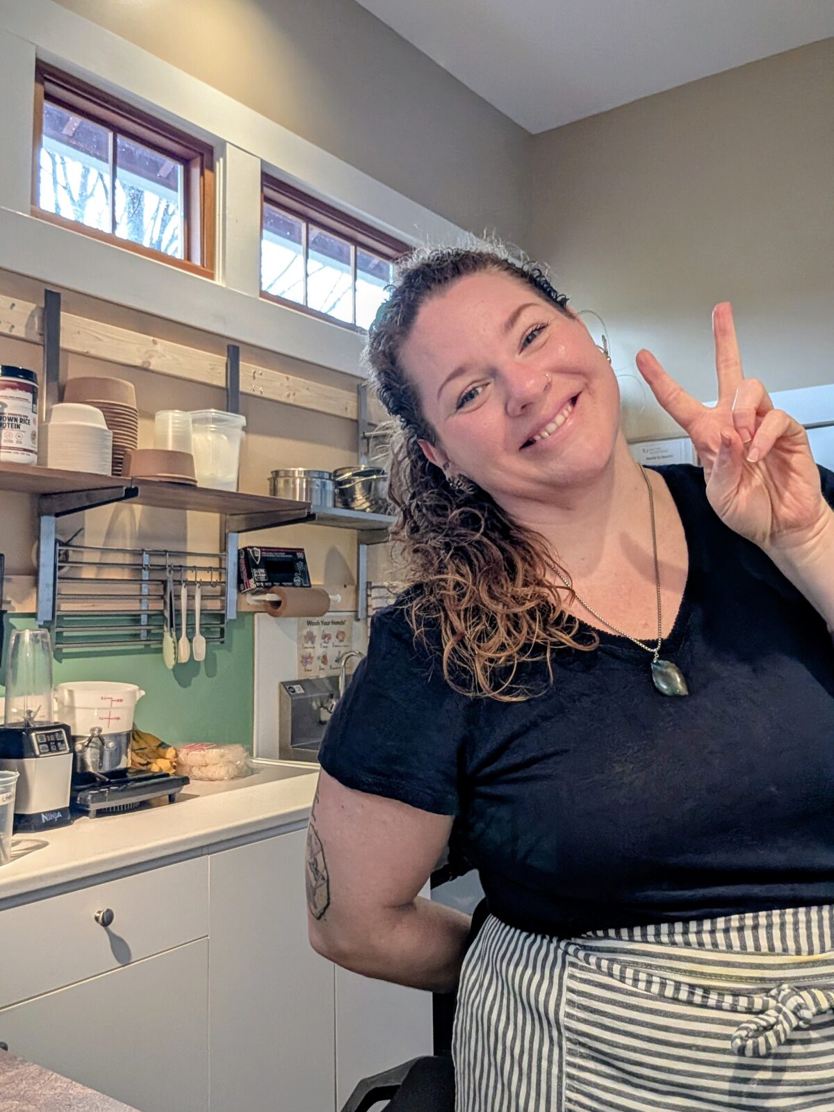 Chef Colleen smiling and giving a peace sign in her OKGN To Go kitchen