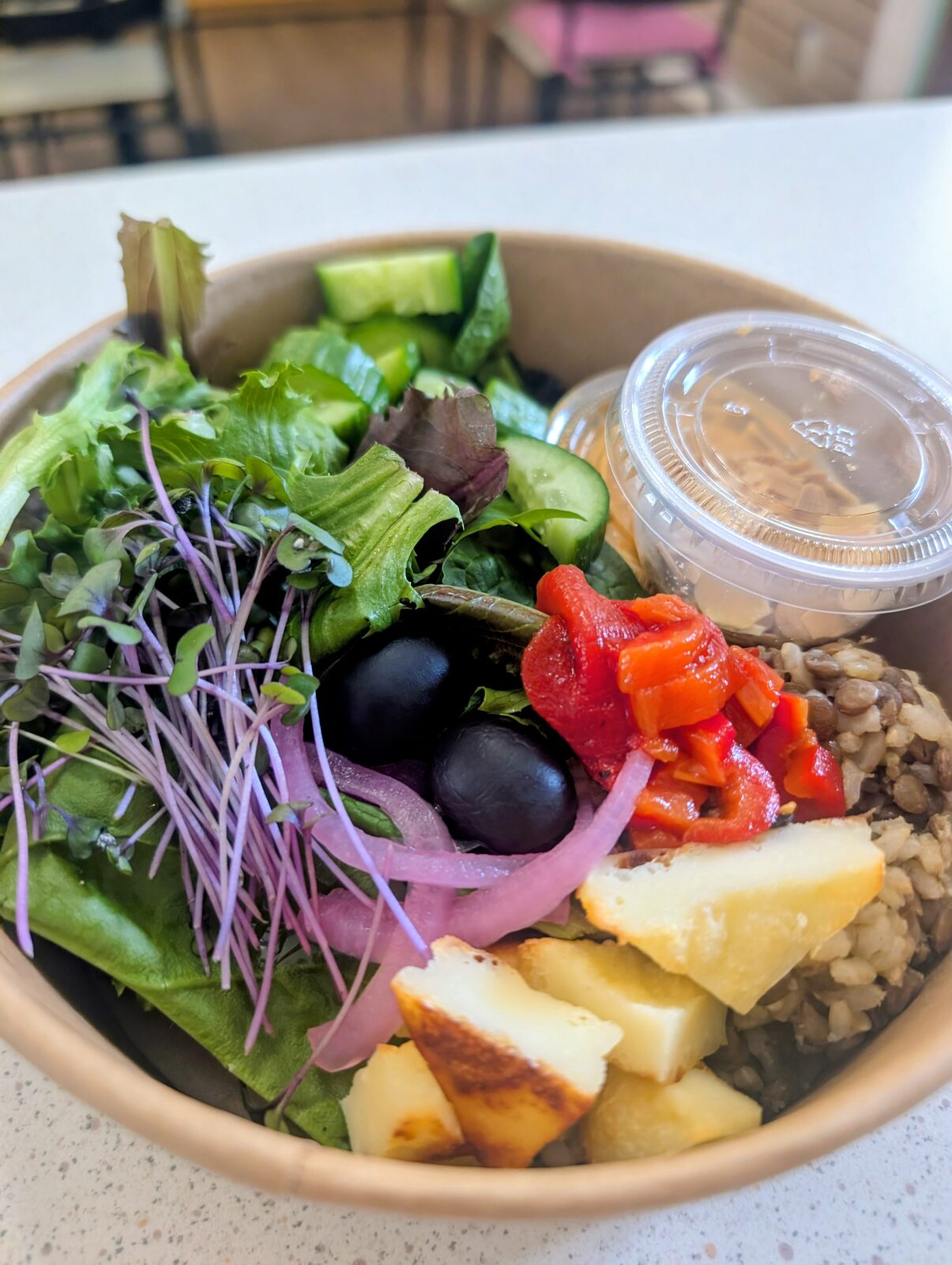 Mediterranean-style bowl with halloumi, cucumber, lentils, microgreens, olives, roasted red peppers and tahini dressing