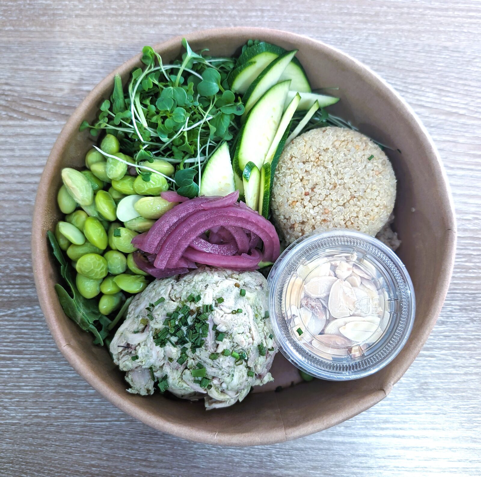 Fresh green bowl with edamame, microgreens, quinoa, pickled onion, and chicken salad