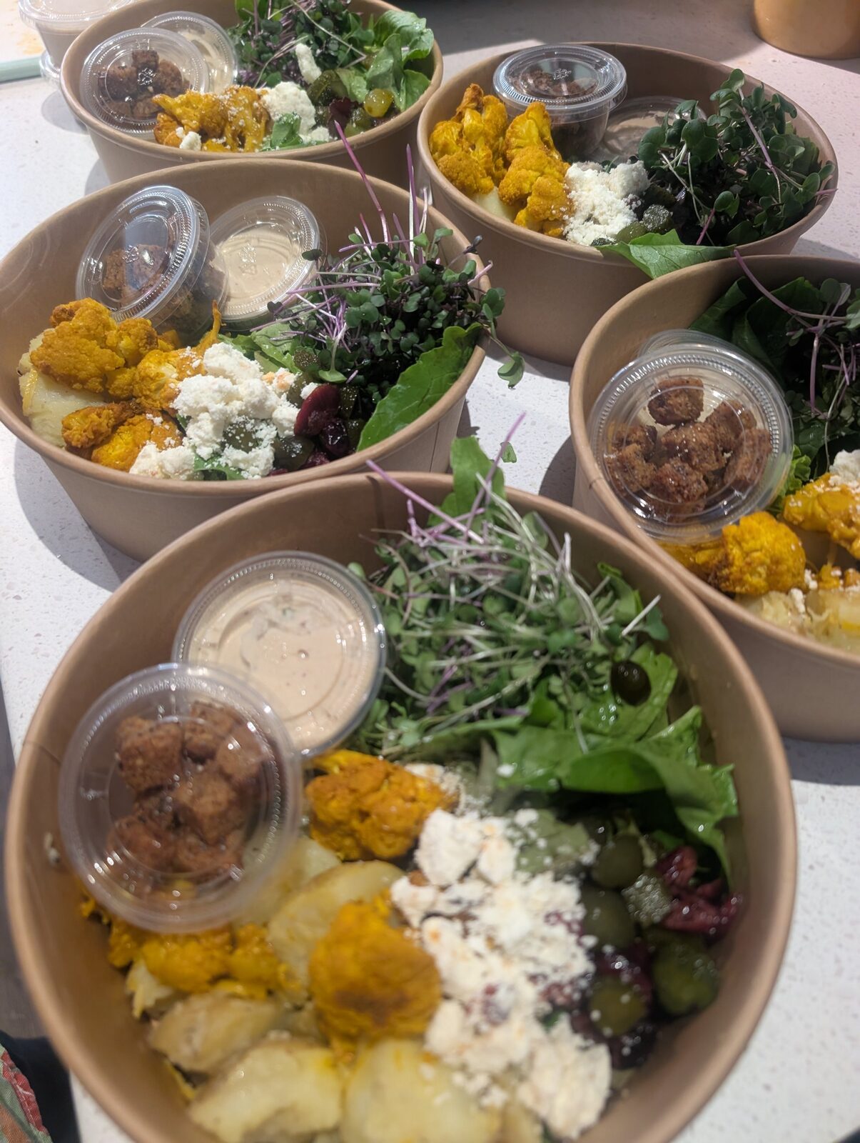 Catering bowls with turmeric cauliflower, feta, olives, microgreens and tahini