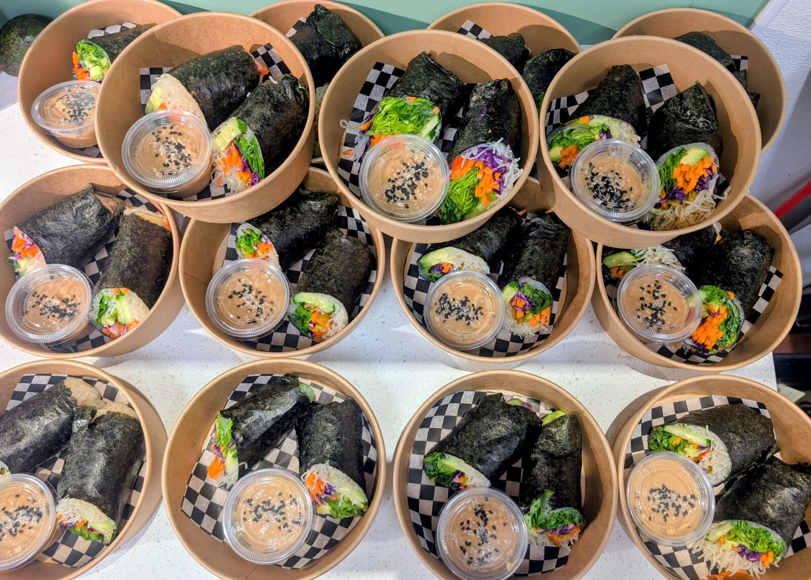 Rows of nori-wrapped sushi bowls with peanut sauce, prepped for a catering order