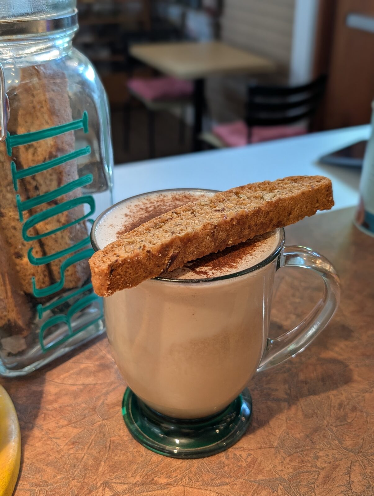 A warm chai latte with cinnamon and a slice of biscotti resting on the rim