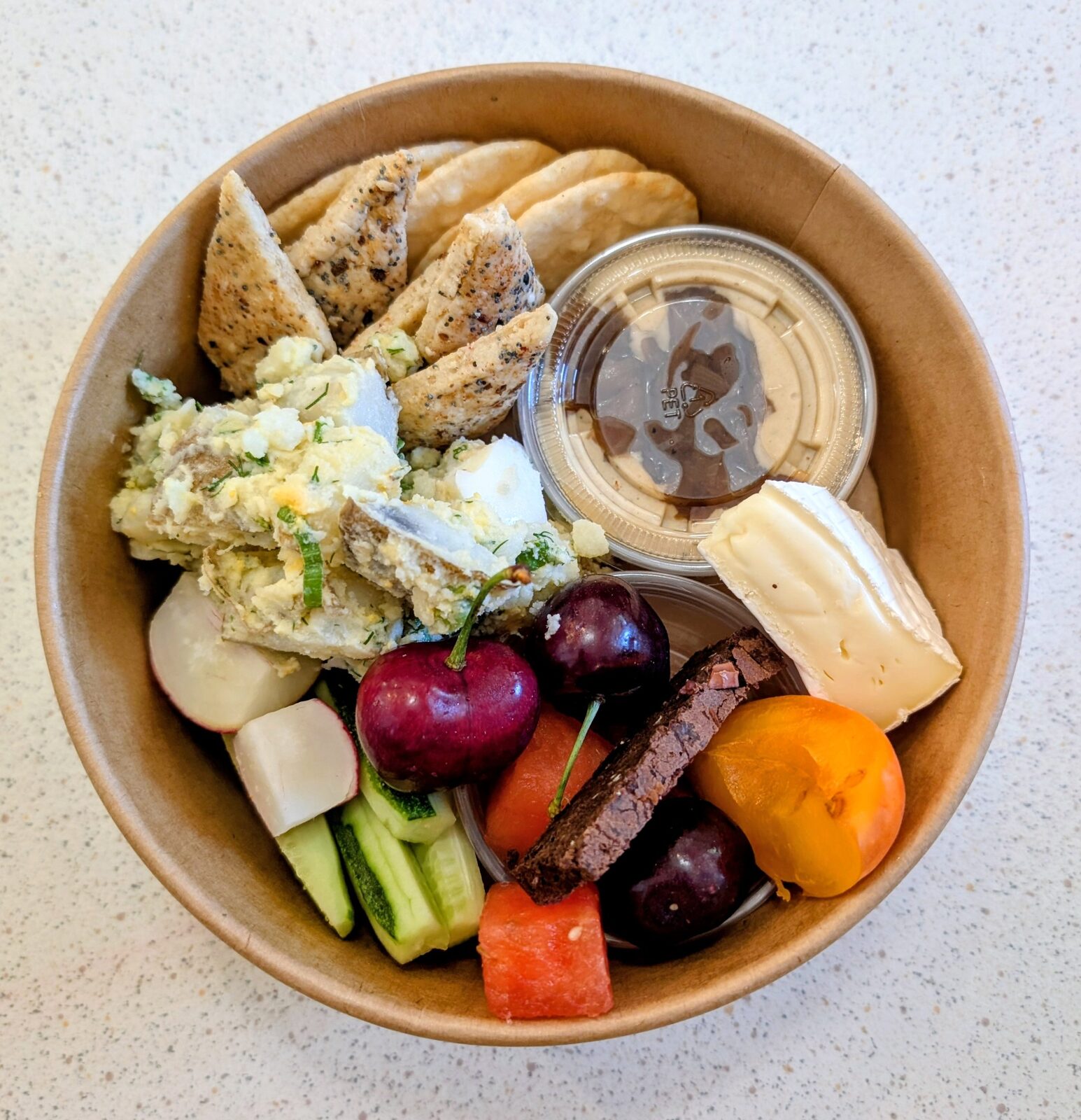 Charcuterie-style lunch bowl with pita, hummus, brie, cherries and fresh fruit