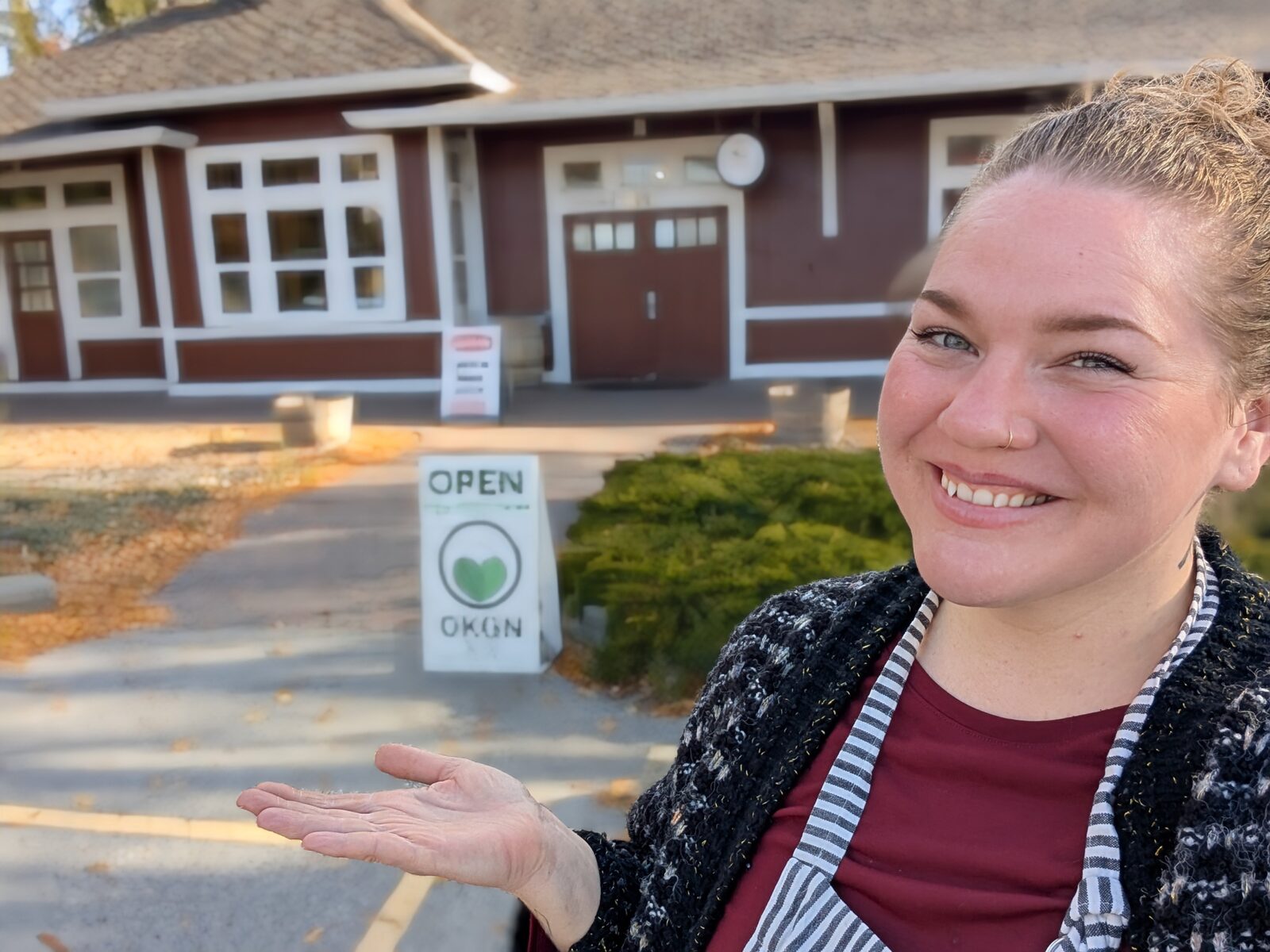 Chef Colleen smiling outside the shop with the OPEN sign and the Visitors Centre behind her