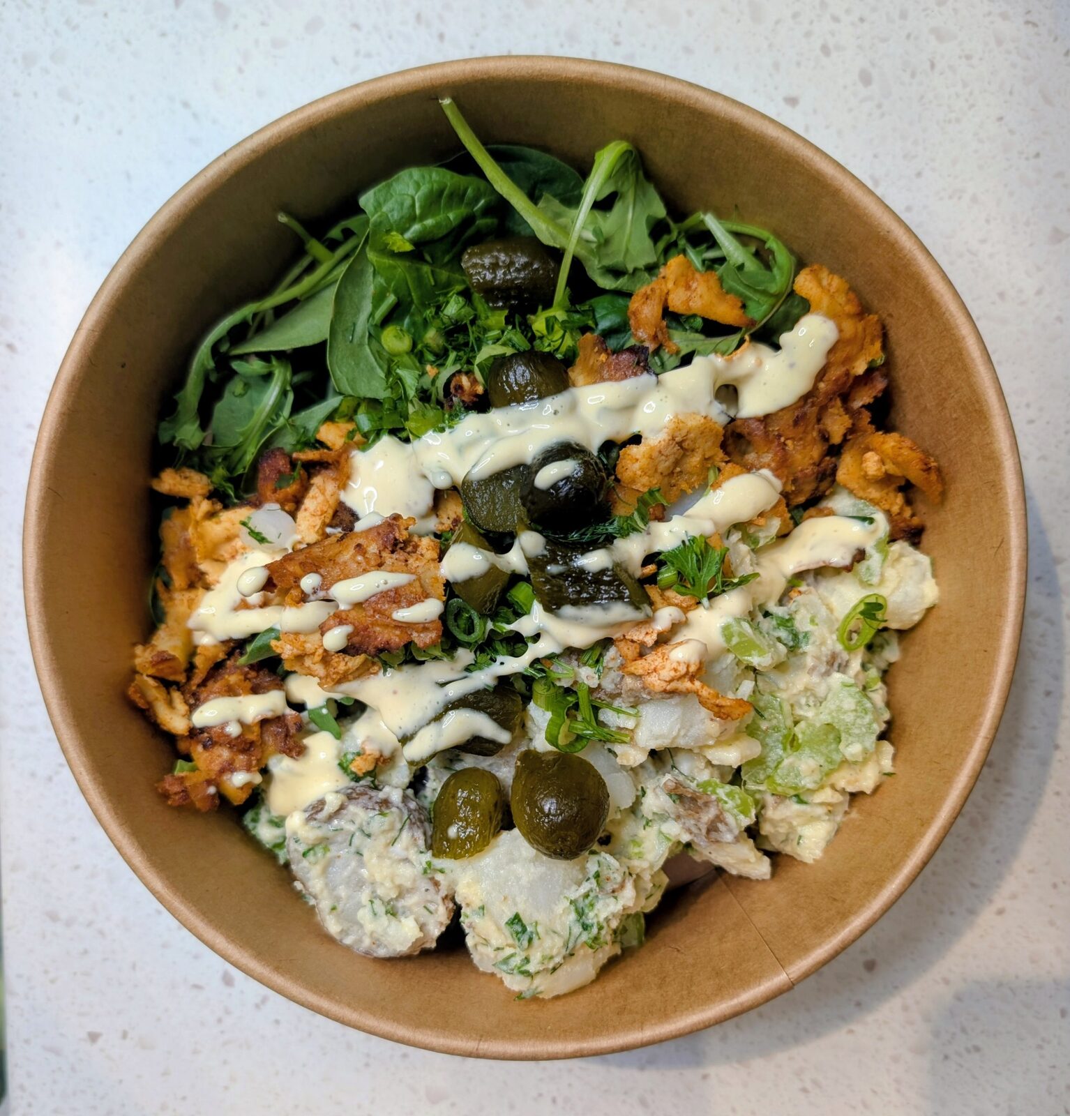 Chicken shawarma bowl with potato salad, pickles, greens and tahini drizzle