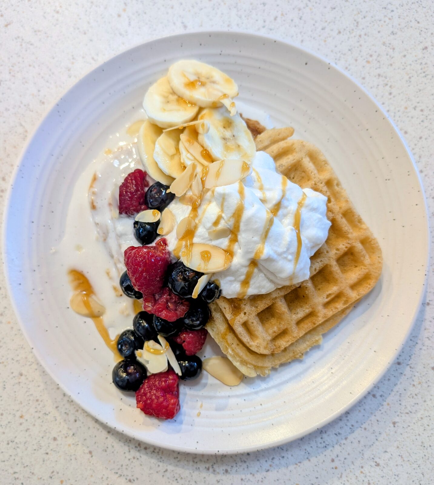 Gluten-free waffle with whipped cream, fresh berries, banana and caramel